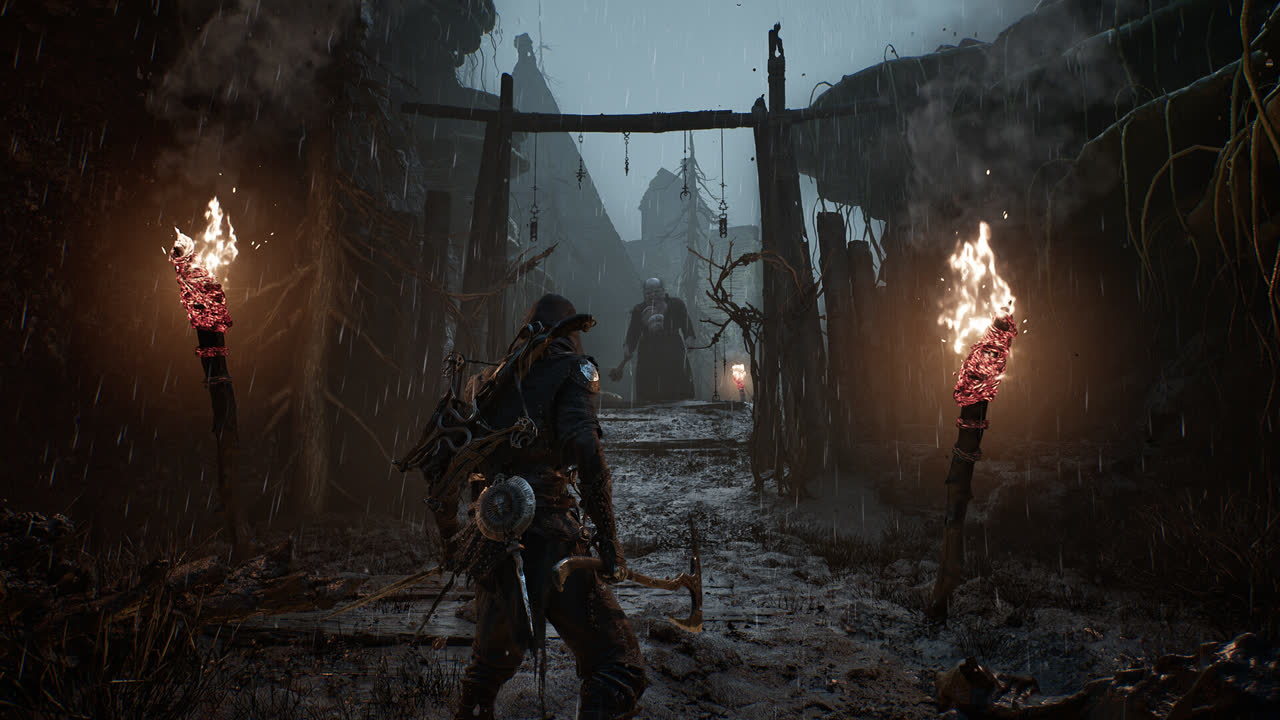 Mortal Shell II official screenshot: a player character advancing between two lit torches through a rain-soaked ruined settlement